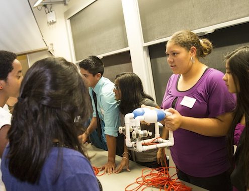 A woman holds a Sea Perch ROV and talks to people at an information table