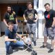 Four male students stand on the dock at the MIT Sailing Pavilion with a surface vehicle resembling a miniature boat that they developed