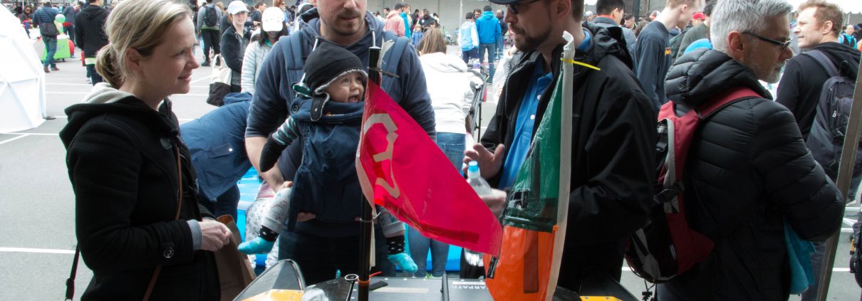 MIT AUV Lab's Paul Robinette talks to a couple with a baby about a yellow AUV on display