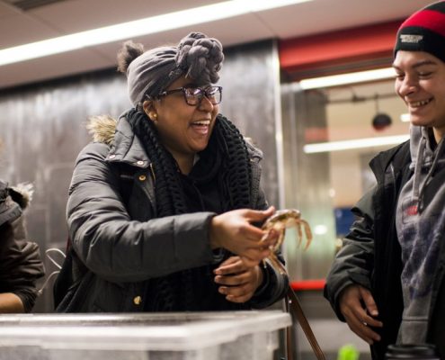 A student holds a crab and laughs while showing a second girl during the High School Marine Science Symposium at Northeastern University