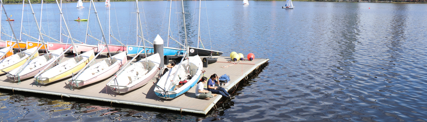 Sailboats on a dock at the MIT Sailing Pavilion with the Boston skyline in the background with the Charles River