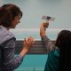 A woman and a child from behind about to drop a cardboard model into a large tank of water.