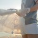 A person holds a plastic bag on the shore of a beach.