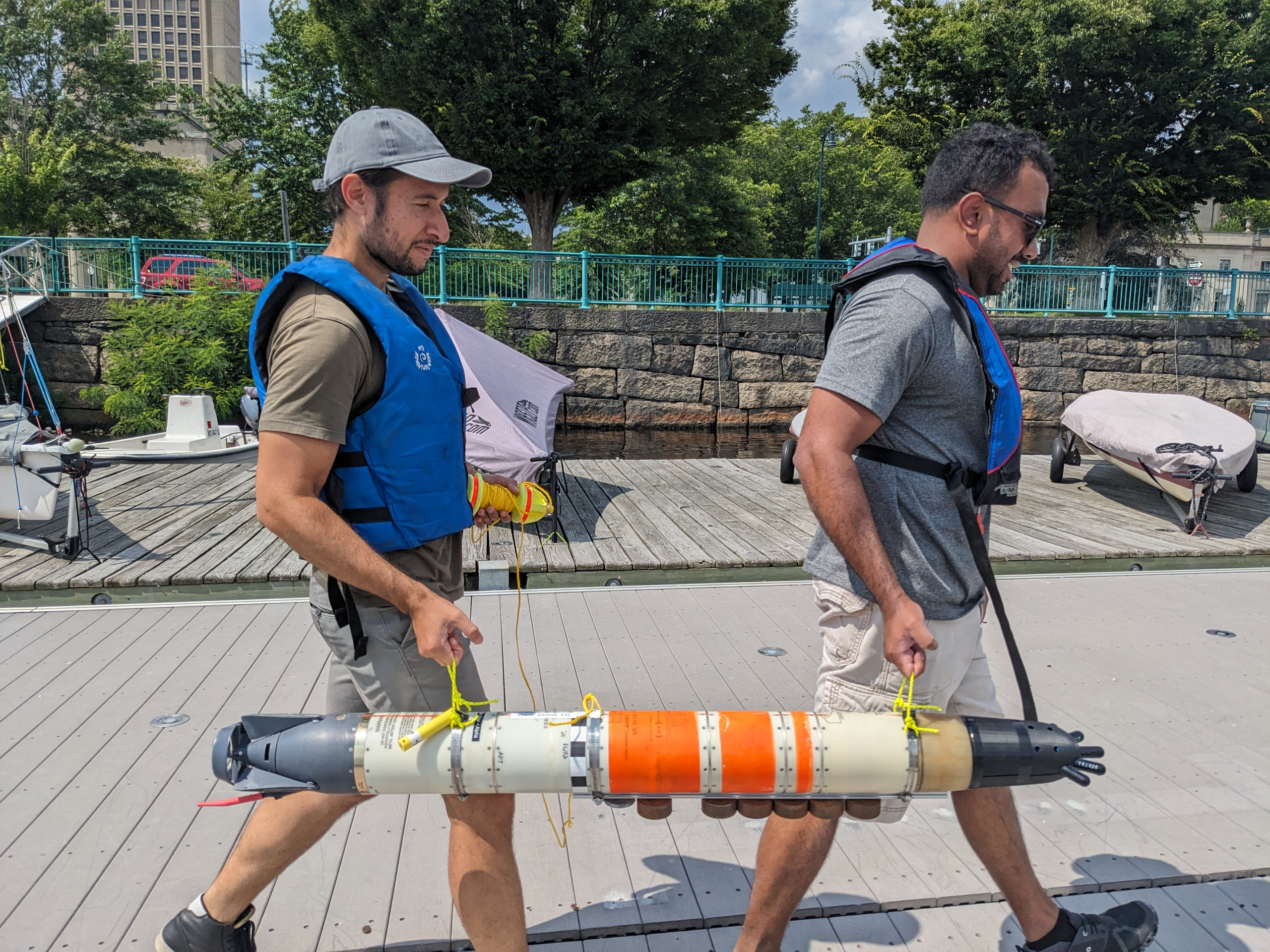 Two MIT Sea Grant researchers wearing life vests carry an underwater vehicle on a dock